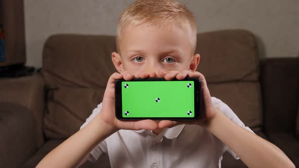 Portrait of a Boy at Home He is Holding a Smartphone with a Green Screen