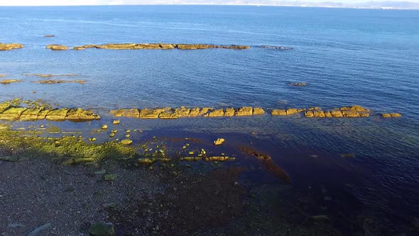 Aerial view of the sea side. Some rocks perfectly aligned on a narrow row are seen. Several paralel