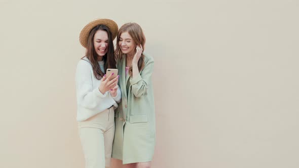 Two young beautiful smiling hipster girls in trendy clothes posing outdoors