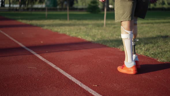 Male Amputee with Prosthetic Legs Walking on Red Sports Track in Summer Park