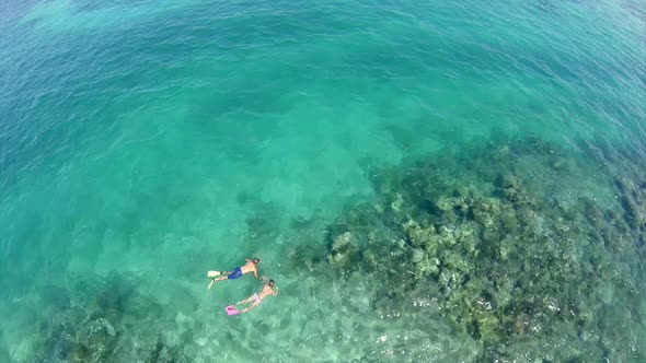 Aerial view of a man and woman couple snorkeling over a coral reef of a tropical island.