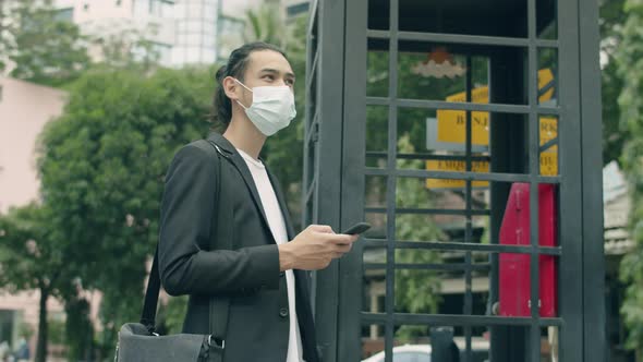 Young Asian businessman using smartphone while standing in the street of the modern city.