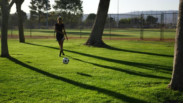 A female soccer player kicking a football to her teammate on a grass sport field.