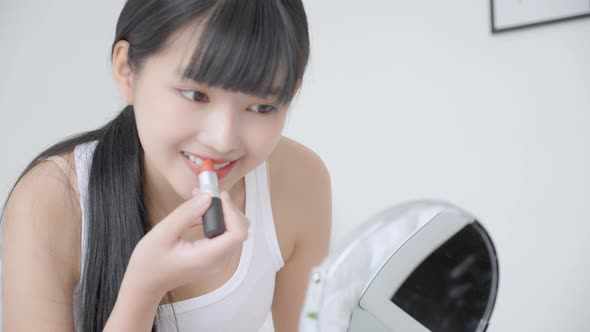 Beautiful young asian woman applying lipstick red on mouth, beauty girl looking facial at mirror.