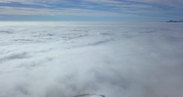 Aerial drone view above the clouds and snow covered mountains in the winter.