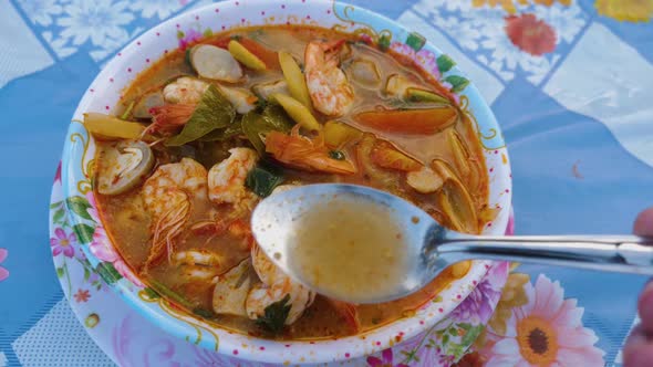 Person tasting lovely Tom Yam Kung soup with spoon.