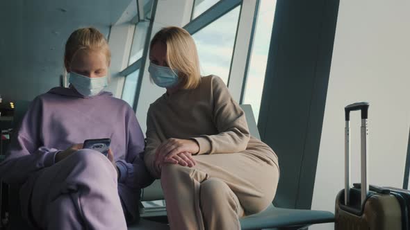 A Woman with a Child is Waiting for a Flight in the Airport Terminal