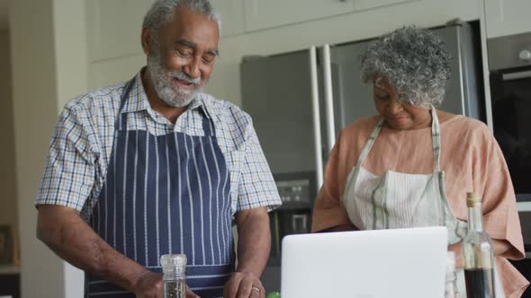 Animation of happy african american senior couple cooking together, using laptop