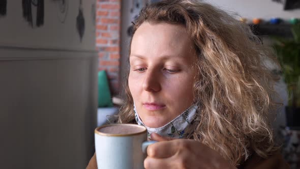 Happy Woman Wearing Face Mask In Cafe Drinking Coffee Or Hot Chocolate. Corona Virus Pandemic