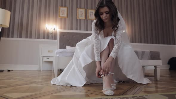 Young Bride in White Wedding Dress Wearing High Heeled Shoes on Slim Legs While Sitting at Home