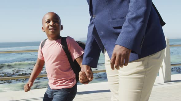 Video of happy african american father and son walking and talking by sea