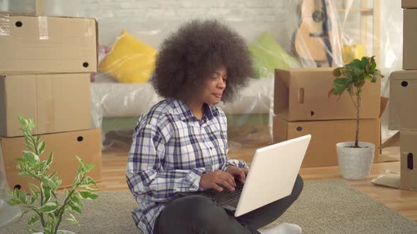 African Woman with an Afro Hairstyle Sitting on the Floor and Using a Laptopconcept of Moving