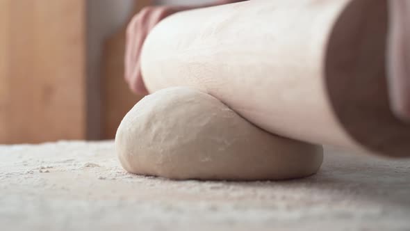 Hands rolling a dough on wooden table. Slow Motion.