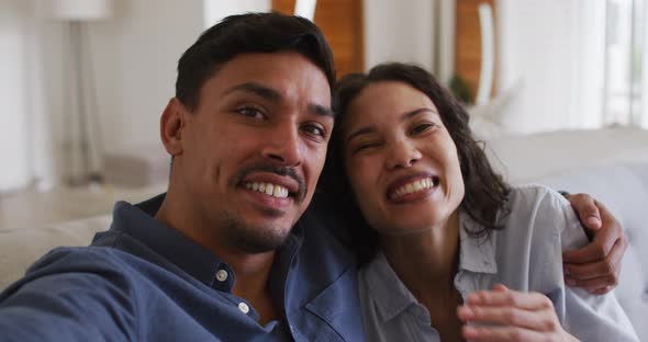 Romantic hispanic couple embracing sending kisses on sofa in living room