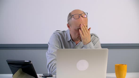 Stressed Businessman Rubbing Face While Sitting with Laptop