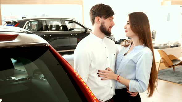 Couple Embraces Each Other Near the Car at the Dealership