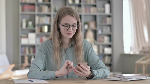 Young Female Student Using Smartphone While Sitting in Study Room