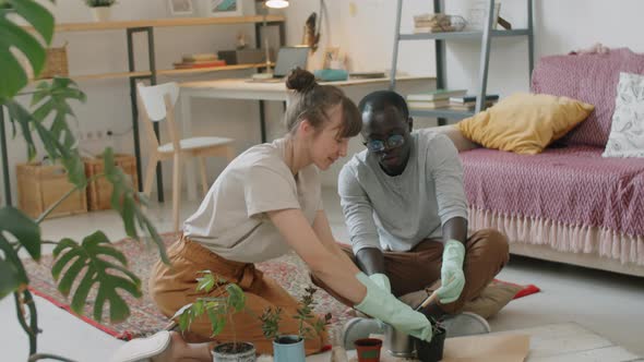 Diverse Couple Repotting Houseplants in Living Room