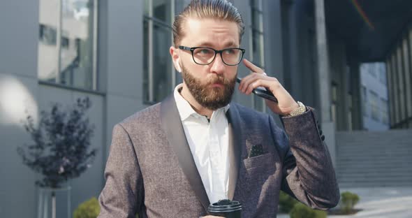 Office Manager in Glasses Checking His Airpods Before Starting to Talk on Smartphone