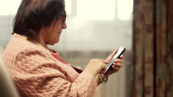 Grandmother In Glasses Scrolling On Screen On Cellphone. Old Granny Using Smartphone For Social.