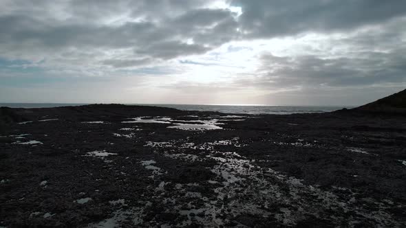 AERIAL: Low dolly towards sea over textured rockpools with sunrays through clouds, Port Eynon Gower,