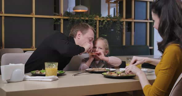 Cheerful Father and Daughter Having Fun Fighting for Pizza Slice in Restaurant