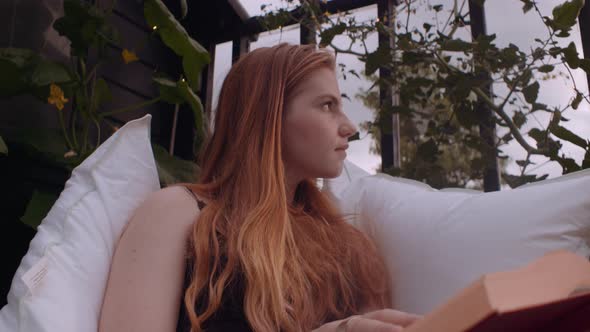 Teenage Girl Sitting Outside On Pillows And Looking Away From Book