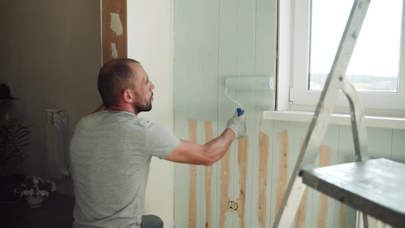 A Man Paints a Wall with a Roller