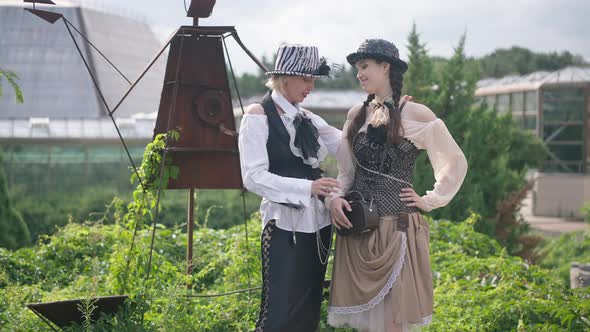 Beautiful Mother and Daughter in Steampunk Costumes Standing Outdoors Talking Smiling