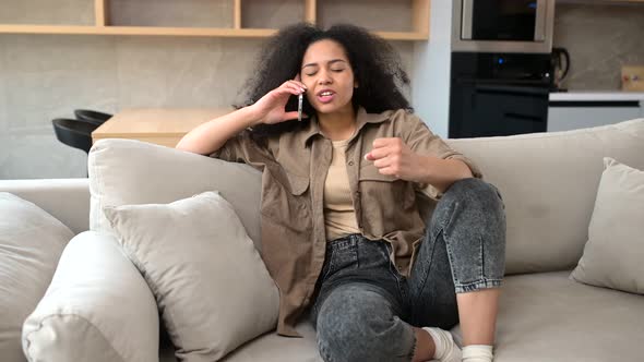 Joyful Multiracial Young Curly Woman Talking Smartphone Sitting on the Sofa