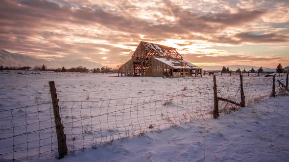 Time-lapse video at sunset with a barn in a snow filled field.