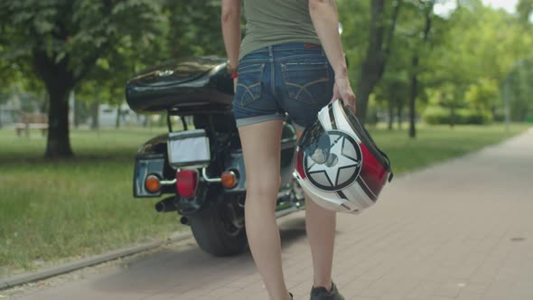 Woman Walking To Motorcycle with Helmet in Hand