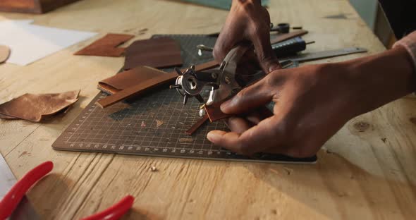 Hands of african american craftsman using tools to make a hole in leather workshop