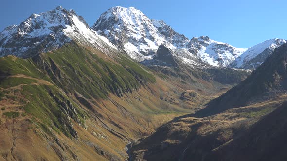 Snowy High Mountain Summit and Autumn Colorful Valley