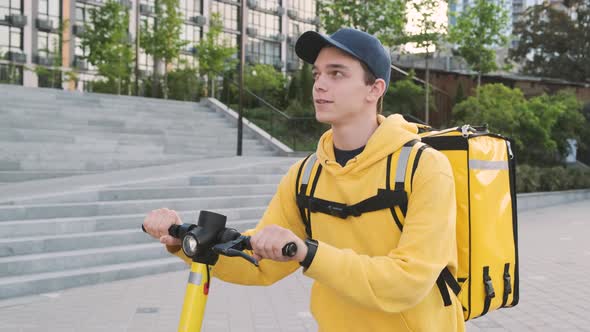 Young Courier with Yellow Backpack Delivers Goods on His Escooter