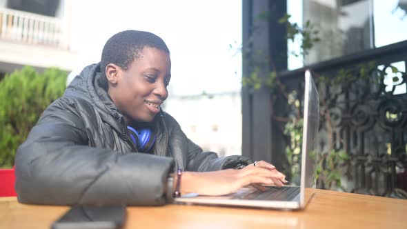 Smiling Happy African Black Shorthaired Woman Student in Black Down Jacket with Blue Headphones