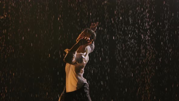 Young Sporty Man Sexy Dancing in the Rain in an Unbuttoned White Shirt. Wet Clothing Hugs 