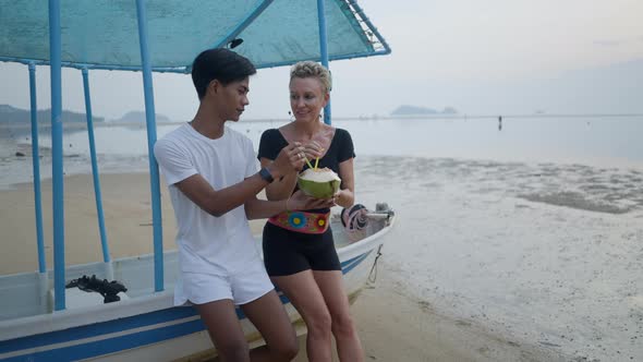 Happy Interracial Couple with Age Differences Drinking Coconut Water Together By the Sea on Vacation