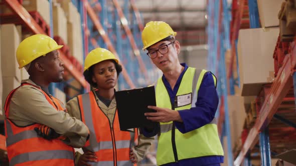 Diverse male and female workers wearing safety suits and talking in warehouse