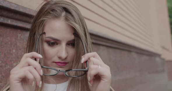 Pretty Girl Wears a Glasses Corrects Hair and Smiles Outdoors at Building