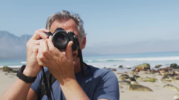 Senior hiker man taking pictures using digital camera on the beach.