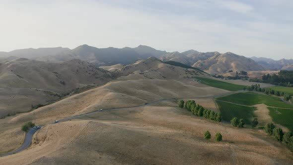 Aerial of dry hills in Marlborough as the vineyards bathe in the sun and three trucks drive along th