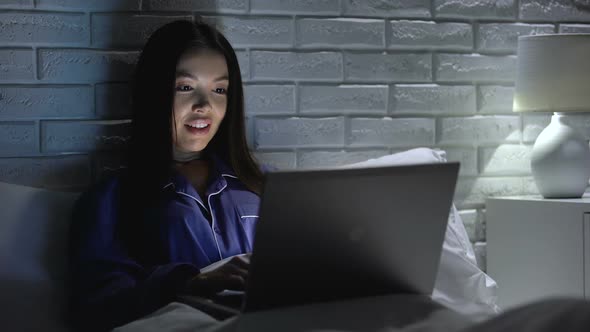 Happy Woman Finishing Project on Laptop at Night, Lying in Bed, Working Overtime