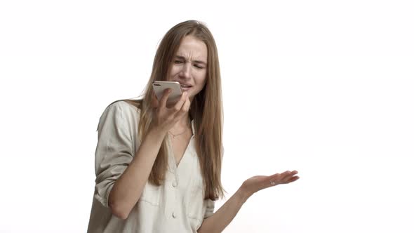 Studio Shot of Adult Woman with Long Fair Hair Wearing Blouse Talking on Speakerphone and Looking