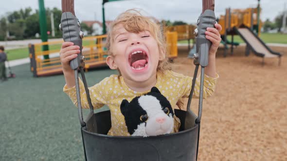 Happy Beautiful Little Girl Lwith Toy Cat Laughing While Swinging at Toddler Swing