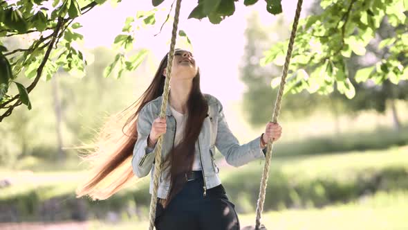 A Young Girl with Long Hair is Swinging on a Rope Swing in the Park