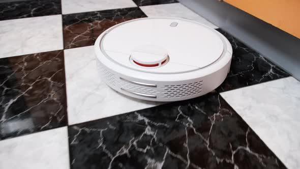 The Robot Vacuum Cleaner Cleans in the Modern House on the Tiles Floor at Kitchen