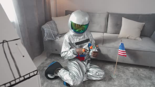 Afro American Man in an Astronaut Costume Sitting on the Floor in Living Room at Home and Playing