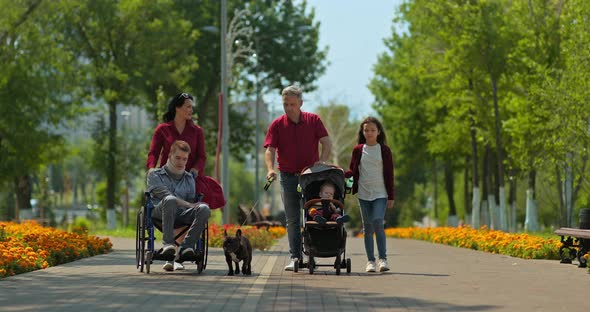 Large Family with a Toddler and a Disabled Teenager Walks Through the Park. Disabled Guy Is Being