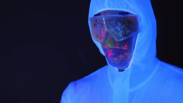 Man in a White Suit with a Mask Splattered with UV Paint Holding a Syringe.